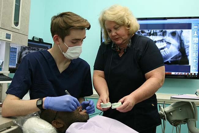牙医在牙医的椅子上监督实习学生和病人