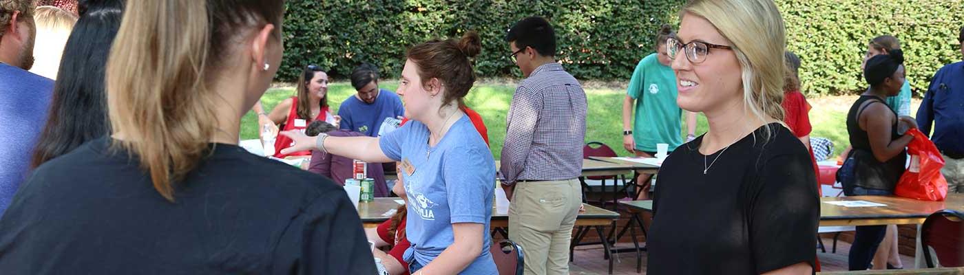 A vendor speaks to students at a busy fair on the college's patio